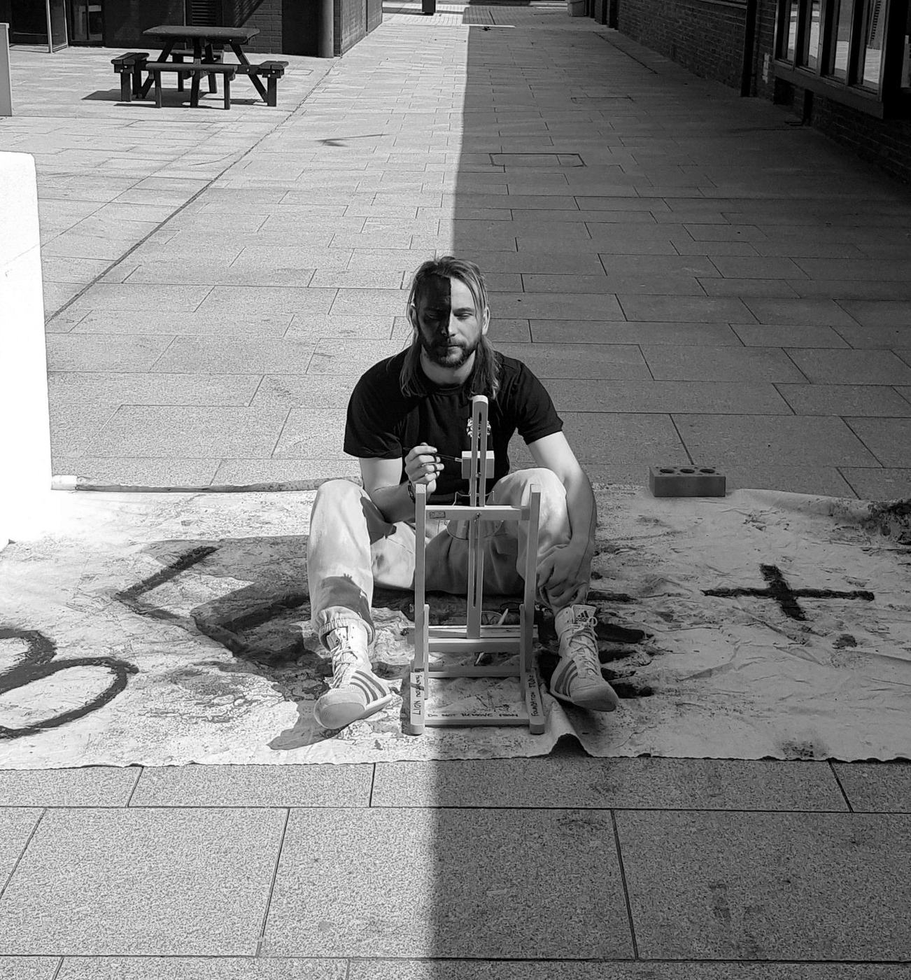 Chance Eaton painting on the ground in Poole, half in sunlight, half in shadow